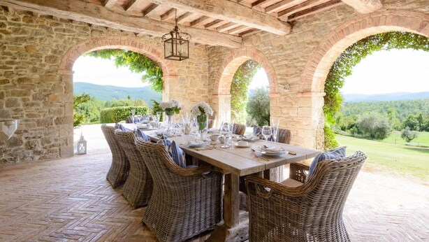 Un espace extérieur abrité, aménagé pour les repas, avec des murs en pierre, des meubles en osier et une vue sur la campagne.
