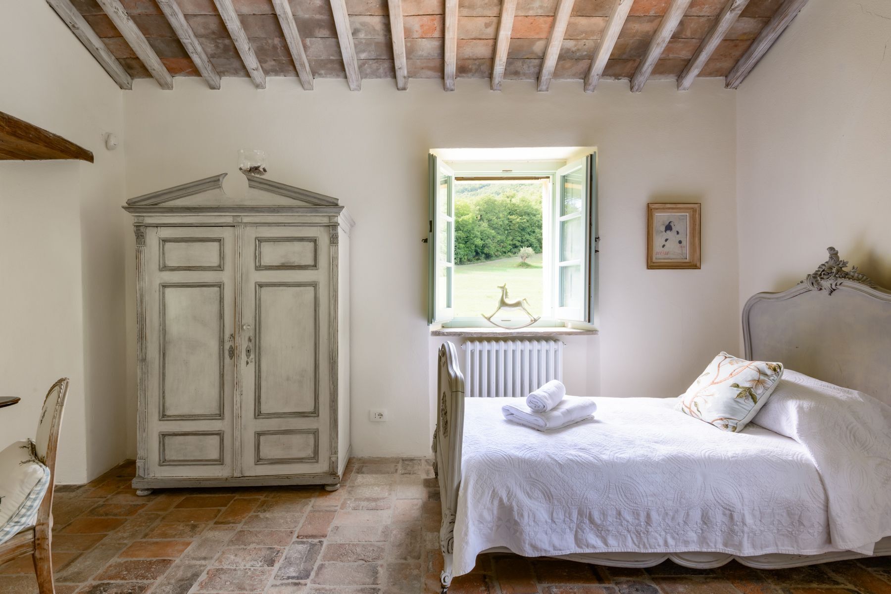 A bedroom with a bed, a white wardrobe, a window with a view, and a radiator.