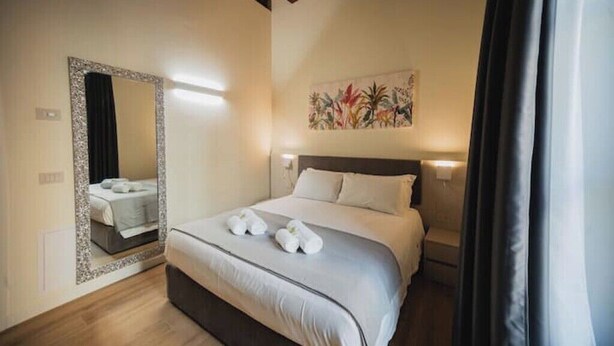Une chambre d’hôtel avec un lit, un grand miroir, un tableau au mur et une fenêtre avec des rideaux.