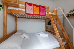 Una cama litera con escalera de madera, ropa de cama blanca y una cortina rojo y naranja.