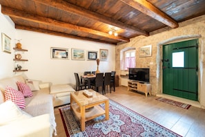 Una sala de estar acogedora con techo de madera, comedor, mueble para televisión y puerta verde.