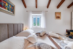 A bedroom with a bed, a window with curtains, a painting on the wall, and a wooden ceiling. - Villa Aurora: A Luxurious Stone Retreat in Dalmatia (Slivno)