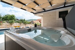 A hot tub with a stone wall backdrop, a pool, and outdoor seating. - Villa Aurora: A Luxurious Stone Retreat in Dalmatia (Slivno)
