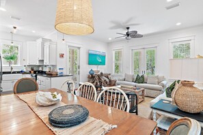 Una cocina moderna con armarios blancos, un comedor con mesa de madera y una sala de estar con sofá y televisor.