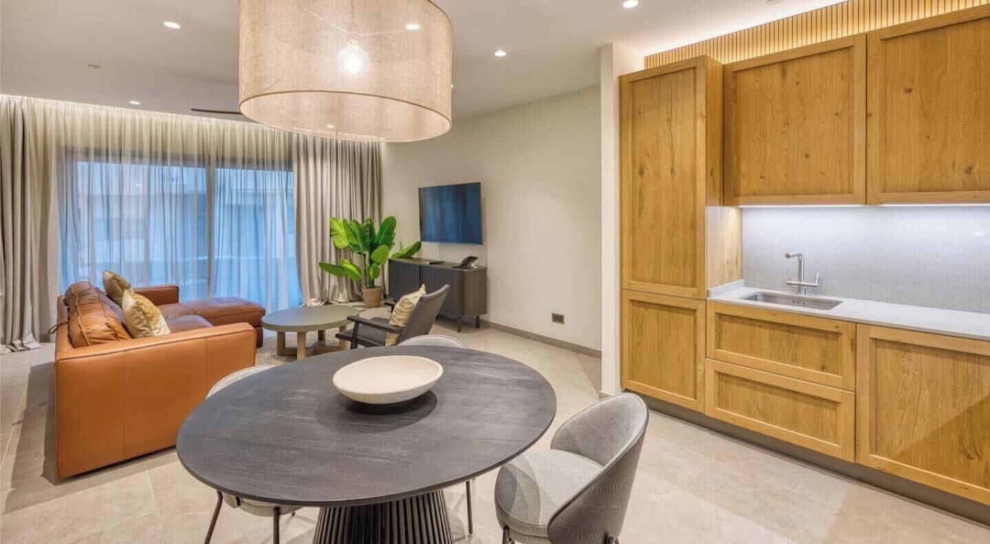 A modern living room with a round table, a sofa, and a kitchen area with wooden cabinets and a sink.