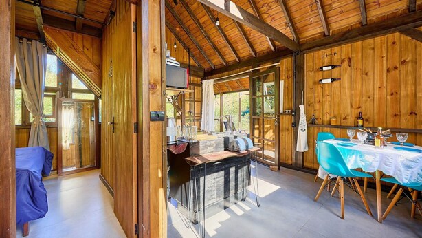 Interior d'una cabana de fusta amb menjador, cuina i una finestra gran.