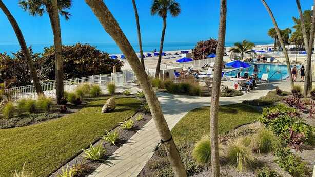 A resort with a pool area, palm trees, and a view of the beach. - Stunning Sand Castle I 308 (Indian Shores)