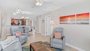 A living room with two armchairs, a coffee table, a ceiling fan, and a kitchen in the background. - Stunning Sand Castle I 308 (Indian Shores)