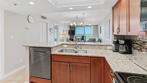 A kitchen with granite countertops, wooden cabinets, a dishwasher, a stove, and a coffee maker. - Stunning Sand Castle I 308 (Indian Shores)
