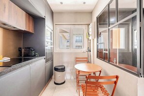 Une cuisine compacte dotée d’appareils électroménagers modernes, un coin repas avec une table et des chaises, et une fenêtre donnant sur des immeubles.