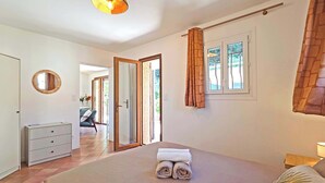 Un dormitorio con cama, cómoda, espejo, ventana con cortinas y puerta que da a otra habitación.