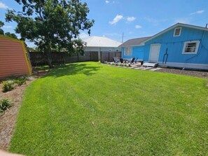 A backyard with a well-maintained lawn, a wooden fence, and a blue house. - Walk to Beach-Backyard with Games-The Blue Marlin (Panama City Beach)