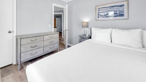 Ein Schlafzimmer mit einem großen Bett, einem Schminktisch, einem Nachttisch und einem gerahmten Bild an der Wand.
