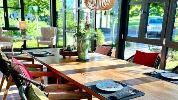 A modern dining area with a long wooden table, chairs, and a hanging light fixture. - Landgut Apfelrose (Friedrichshafen)