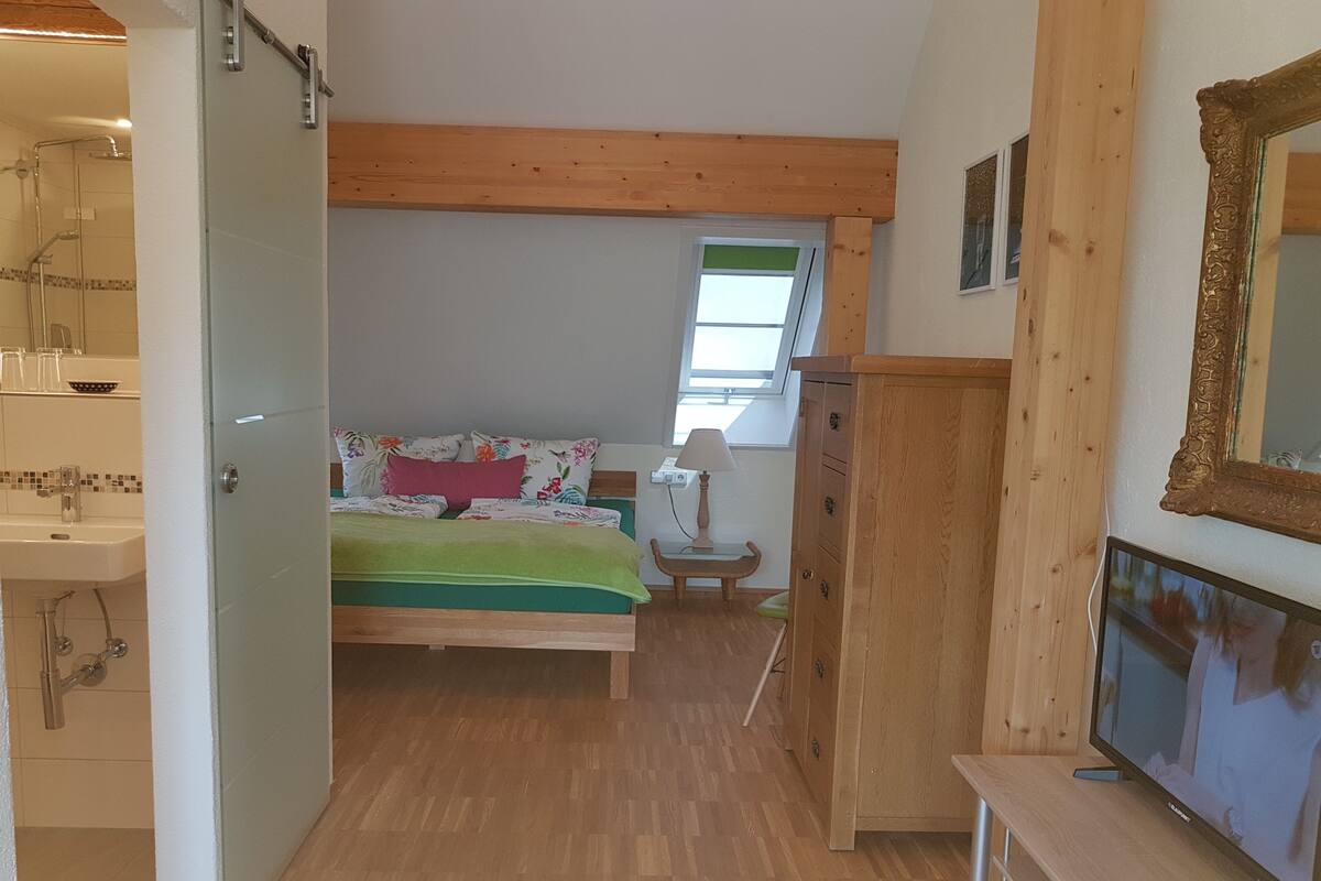 A bedroom with a bed, a wooden wardrobe, a television, and a window with a view.