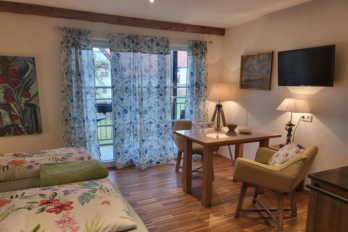 A room with a bed, a dining table with chairs, a lamp, and a TV.
