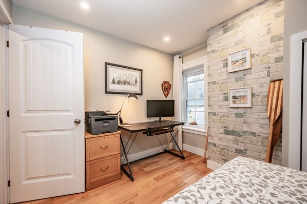 A bedroom with a bed, a desk with a computer, a dresser, and a window.