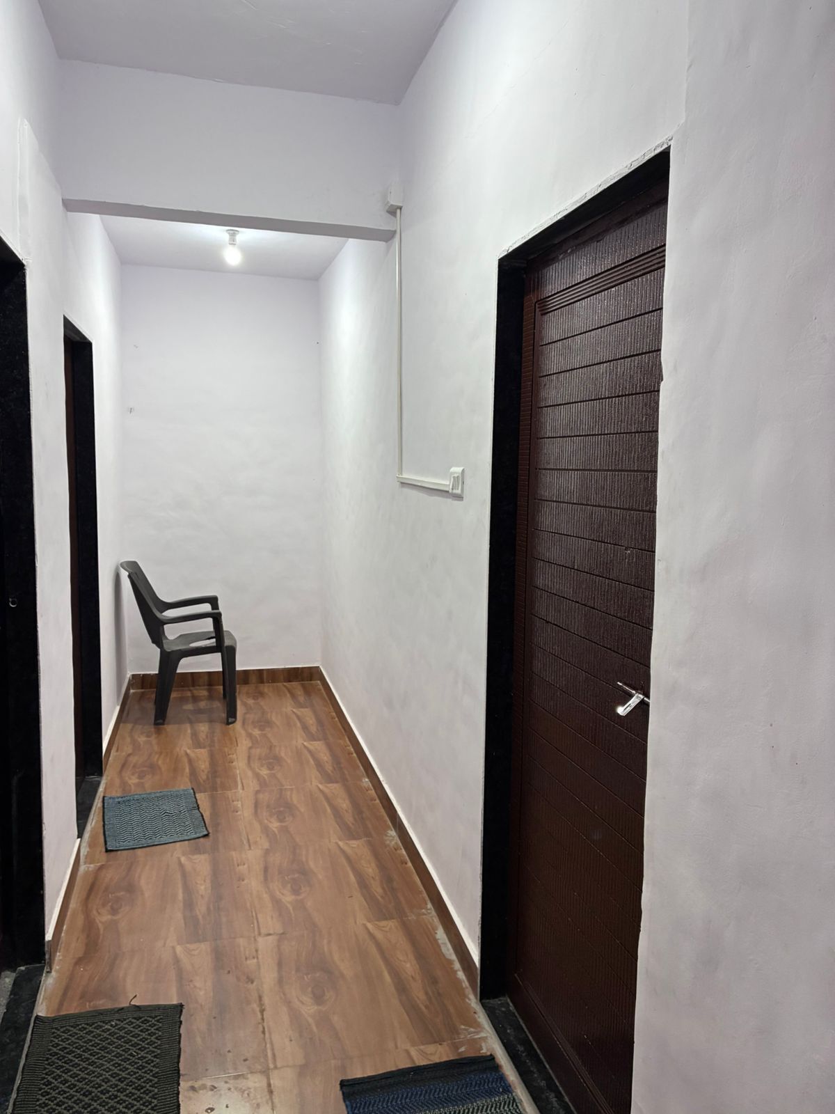 Un pasillo estrecho con suelo de madera, una puerta negra y una pared blanca.