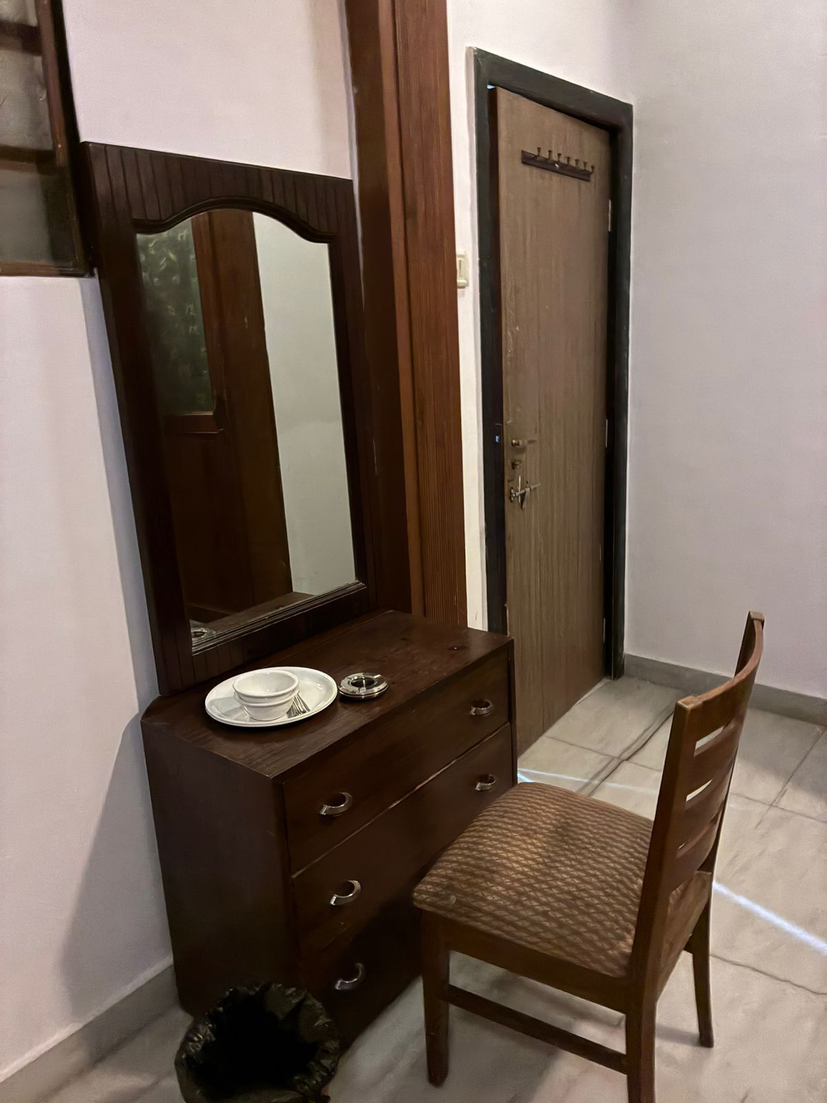 Een houten dressoir met spiegel, een stoel en een deur in een kamer met betegelde vloer.