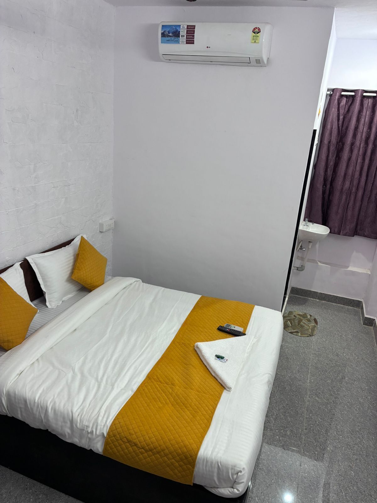 Habitación de hotel con una cama, un control remoto, una toalla, un lavamanos y una cortina de ducha.