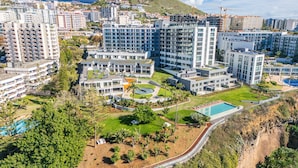 A modern residential complex with multiple high-rise buildings, a central courtyard with a swimming pool, and a hillside backdrop. - Acqua Gem by Homie in Funchal (Funchal)