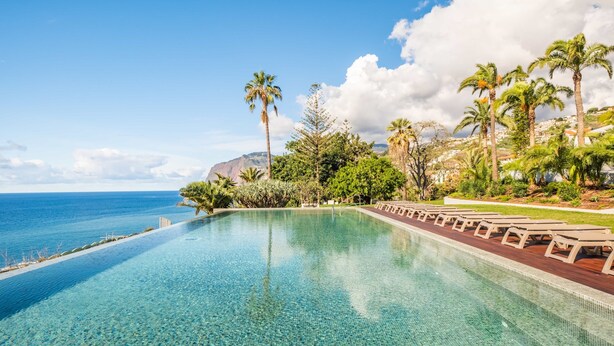 A clear blue pool with lounge chairs, palm trees, and a view of the ocean. - Acqua Gem by Homie in Funchal (Funchal)