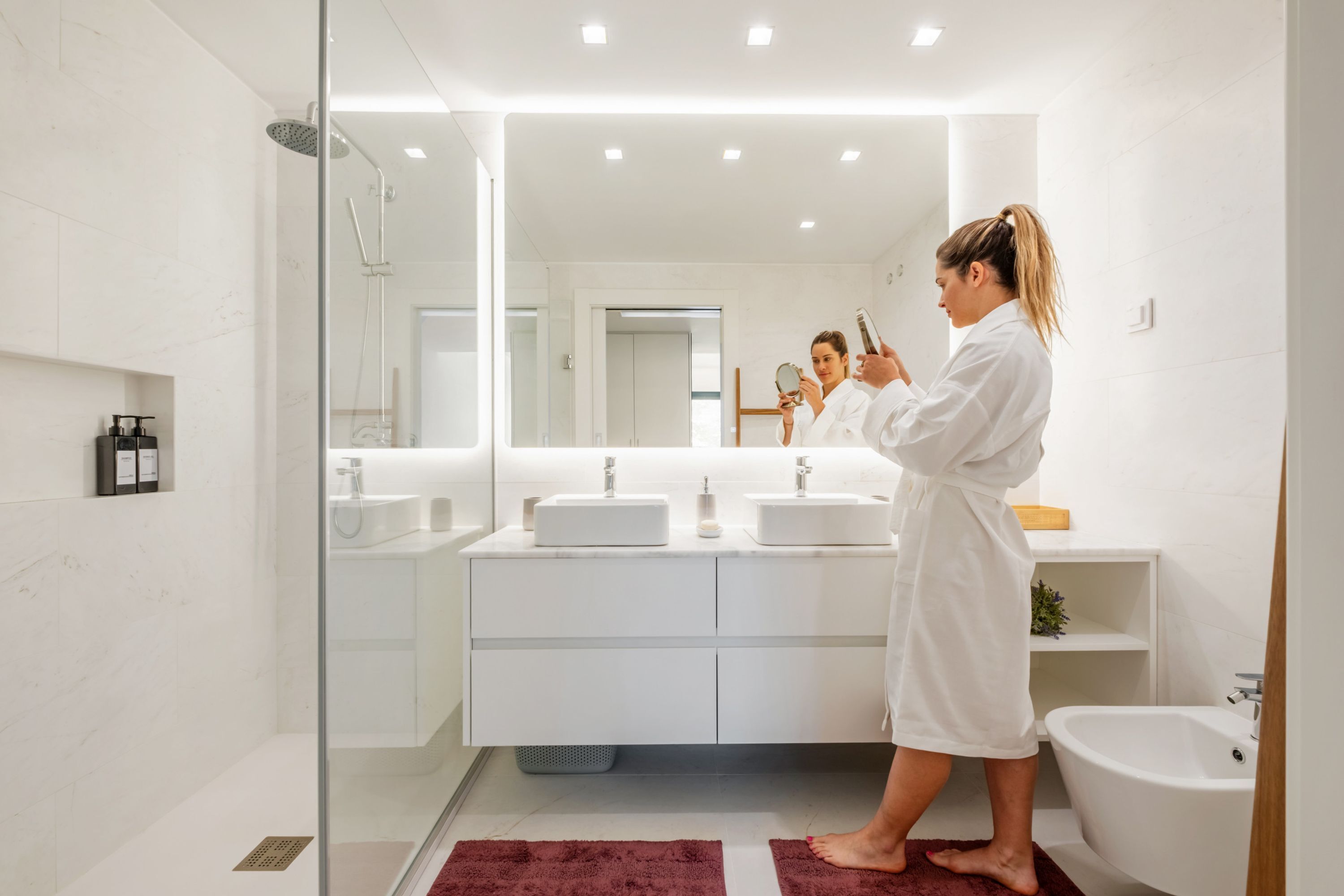 Ein modernes Badezimmer mit einer Duschkabine aus Glas, einem großen Spiegel und einem weißen Waschtisch mit zwei Becken.