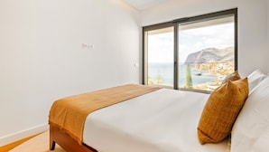 A bedroom with a bed, a window with a view of a mountainous landscape, and a wooden floor. - Acqua Gem by Homie in Funchal (Funchal)