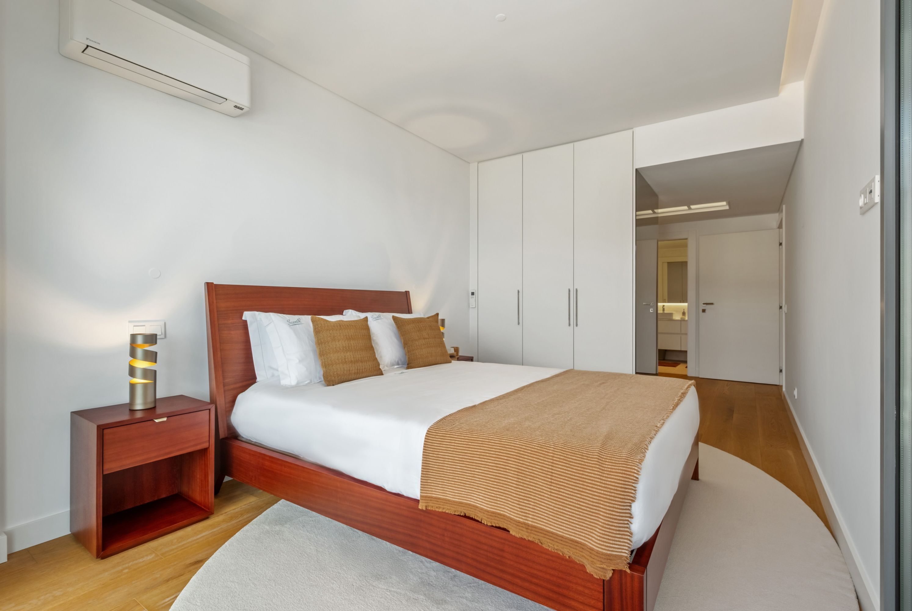 Une chambre à coucher avec un lit en bois, du linge de lit blanc, une table de chevet avec une lampe et une armoire.