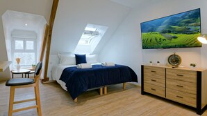 A bedroom with a bed, a desk, a chair, a dresser, and a TV mounted on the wall.