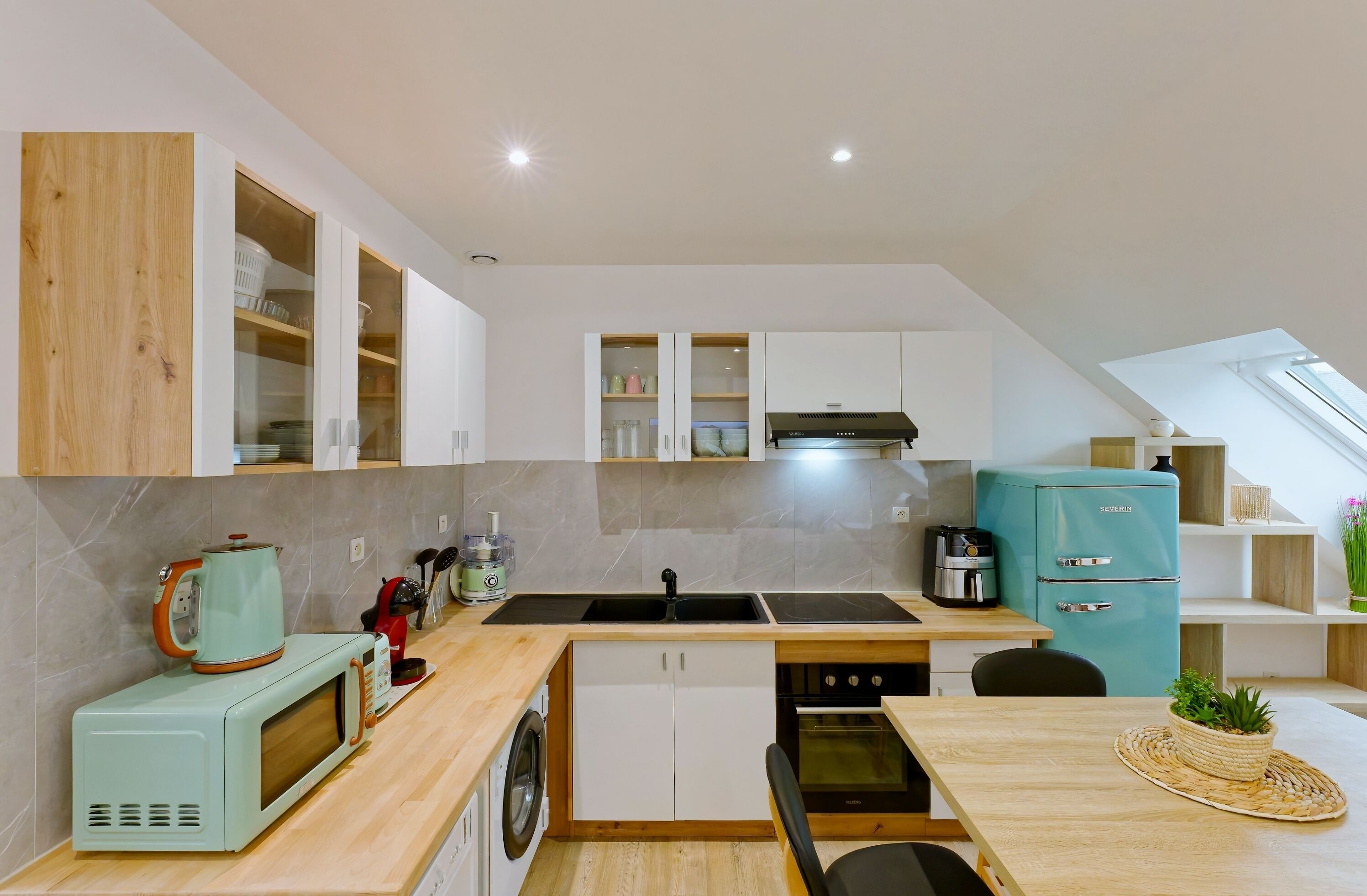 A modern kitchen with a built-in microwave, sink, and stove. There is a washing machine and a teal refrigerator.