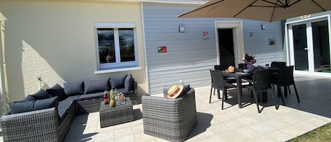 A patio with wicker furniture, a table with drinks, and a large umbrella.