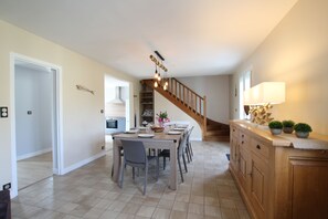 A dining area with a wooden table set for six, a staircase, and a kitchen in the background. - 200 meters from the beach with access to a heated pool – Family-friendly vacation rental (Port-Bail-sur-Mer)