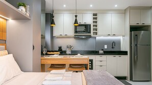 Een moderne hotelkamer met een bed, een zithoek met tafel en stoelen, een keuken met apparatuur, en een klein balkon.