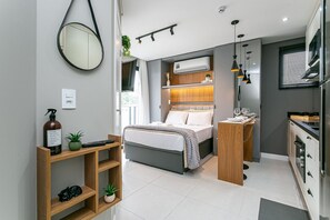 Ein modernes Schlafzimmer mit Bett, Nachttisch und einer kleinen Holzablage mit Pflanze und Flasche.