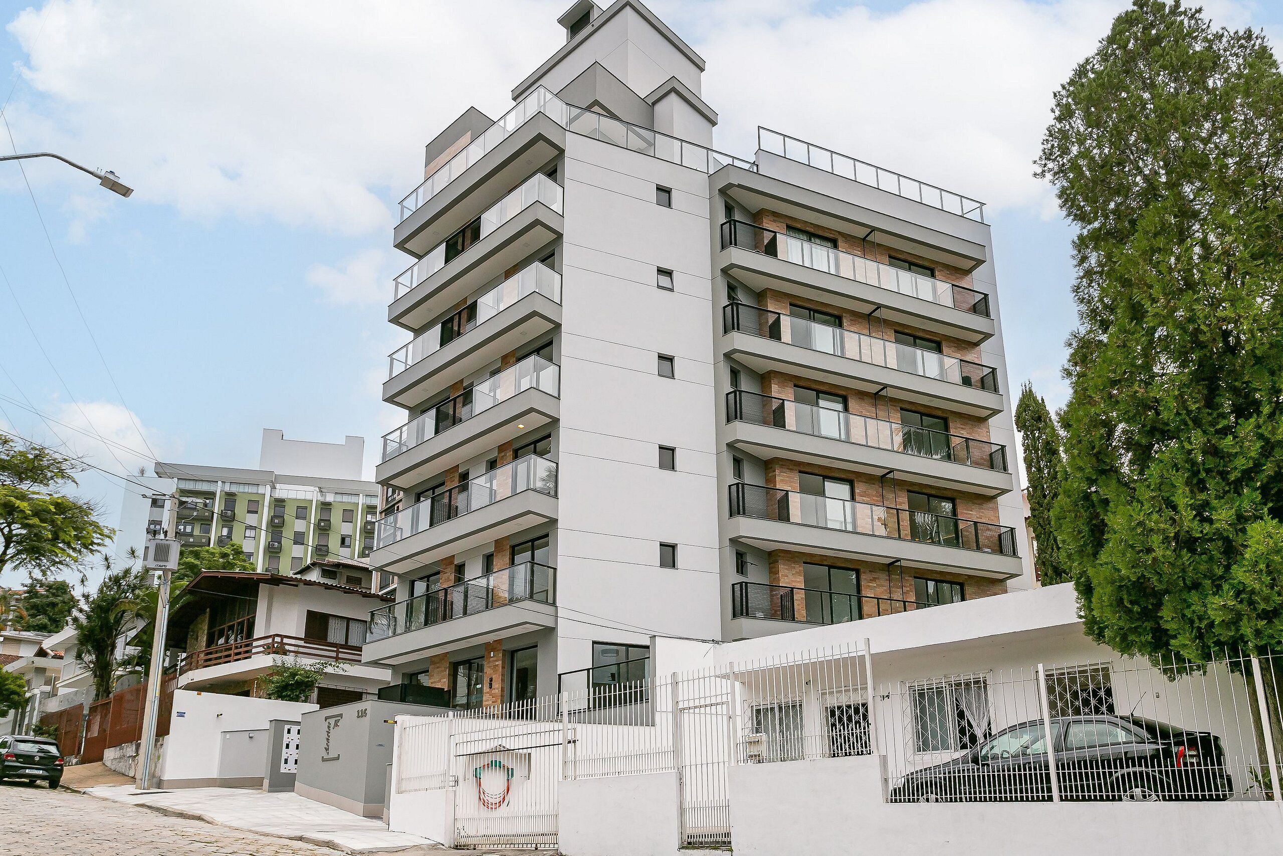Un immeuble résidentiel à plusieurs étages, doté de balcons, d’une entrée sécurisée et d’une voiture garée.