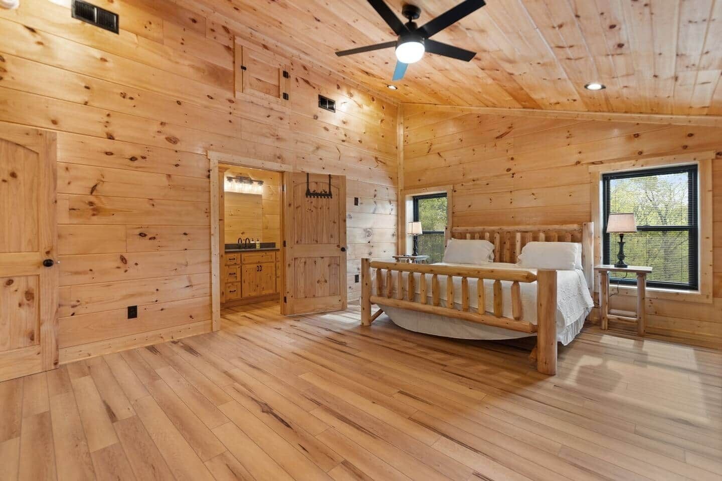 A wooden cabin interior with a bed, a ceiling fan, and a window.