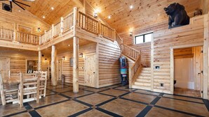 A log cabin interior with a central staircase, a dining area, and a bear statue. - Shawnee Creek Bourbon Trail Chalet (Mercer County)