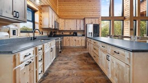 A log cabin-style kitchen with wooden cabinets, a black countertop, and a large window. - Shawnee Creek Bourbon Trail Chalet (Mercer County)