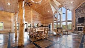 A spacious log cabin interior with a large dining table, a fireplace, and large windows. - Shawnee Creek Bourbon Trail Chalet (Mercer County)