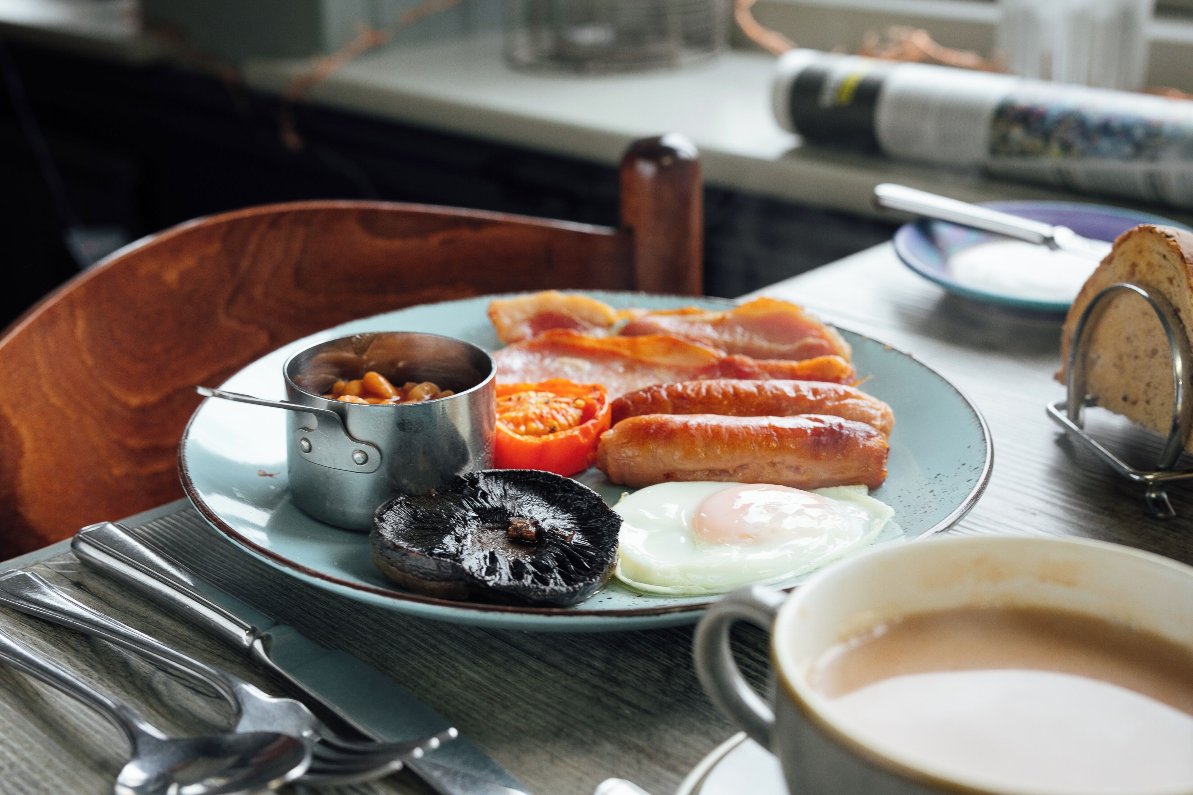 Un piatto colazione con uova, pancetta, salsiccia e una piccola ciotola di fagioli.