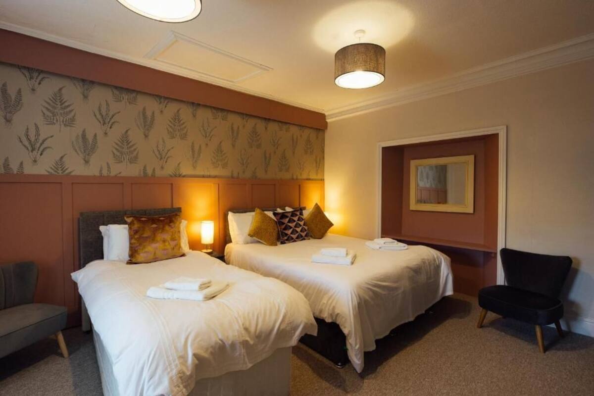 A hotel room with two beds, a chair, a lamp, and a framed picture on the wall.