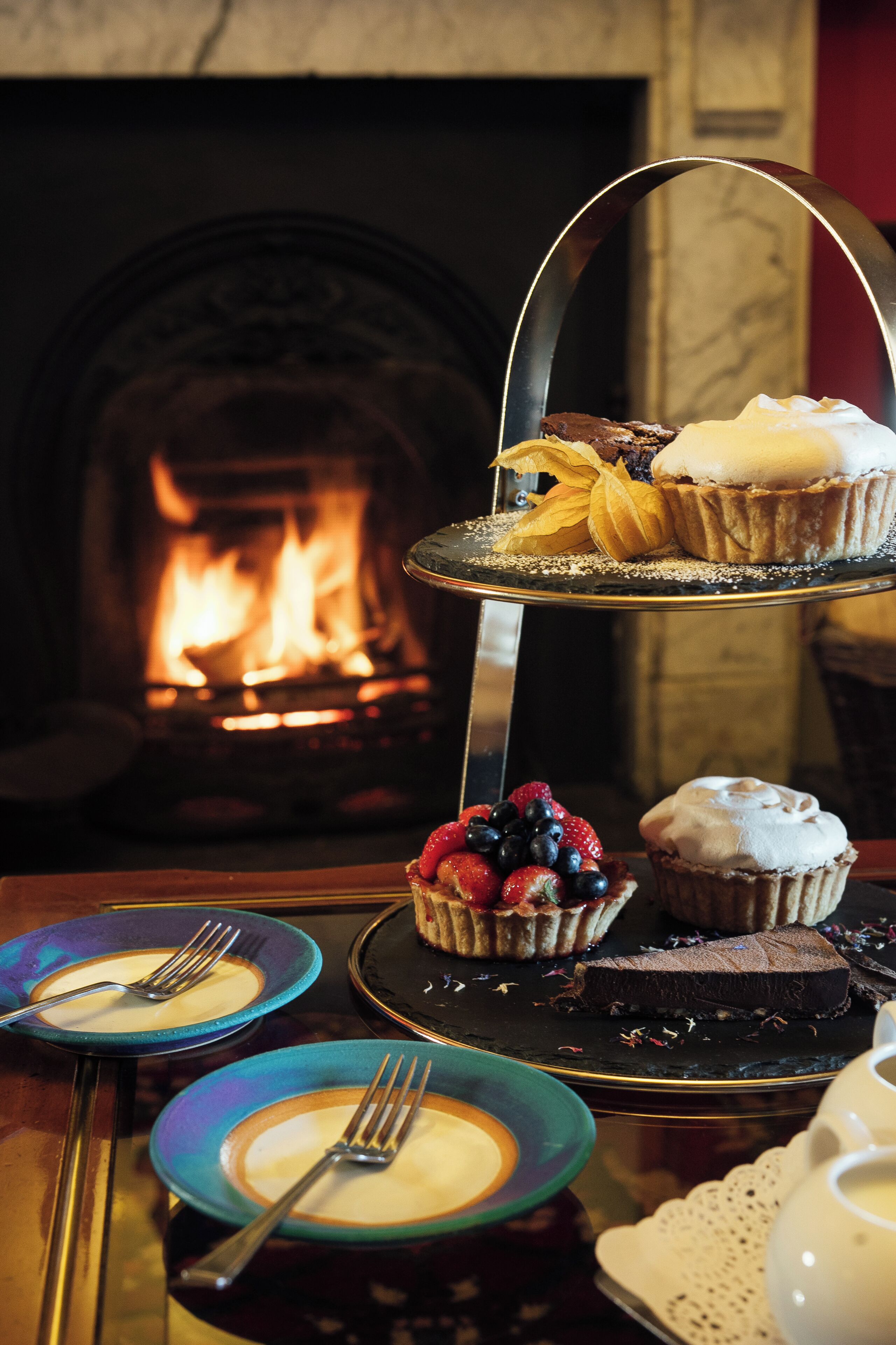 Un présentoir à étages garni de diverses pâtisseries et de fruits, placé devant une cheminée.