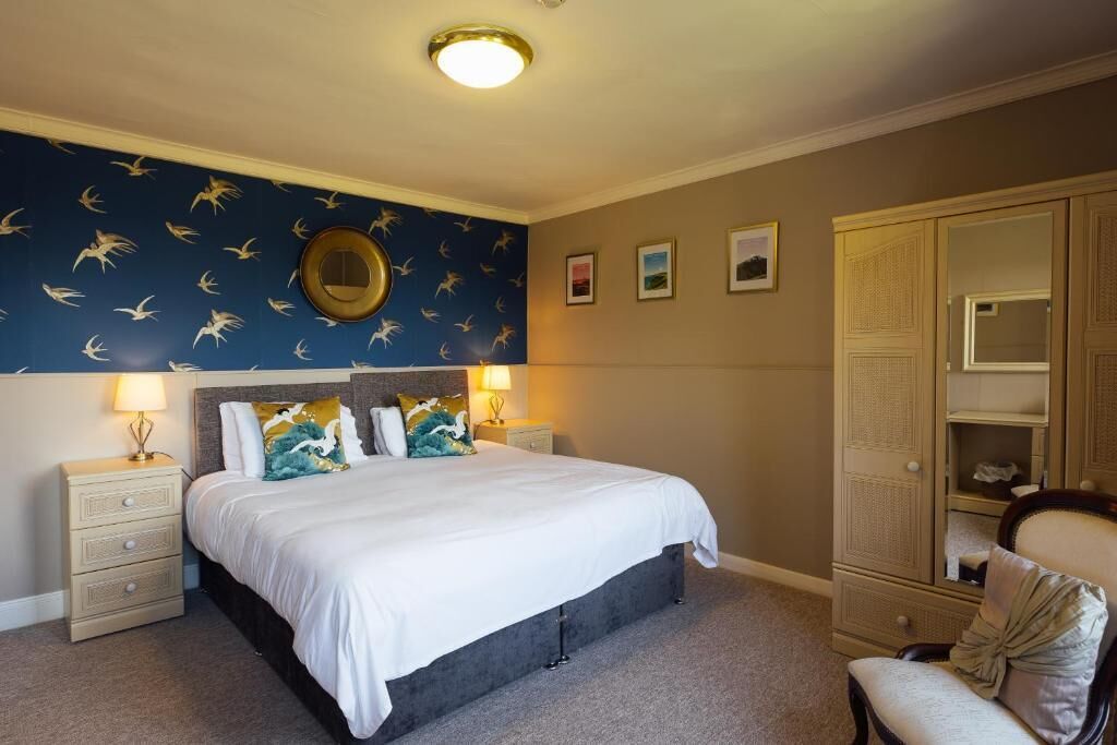 A bedroom with a bed, nightstands, a dresser, a chair, and a wall with a circular mirror.