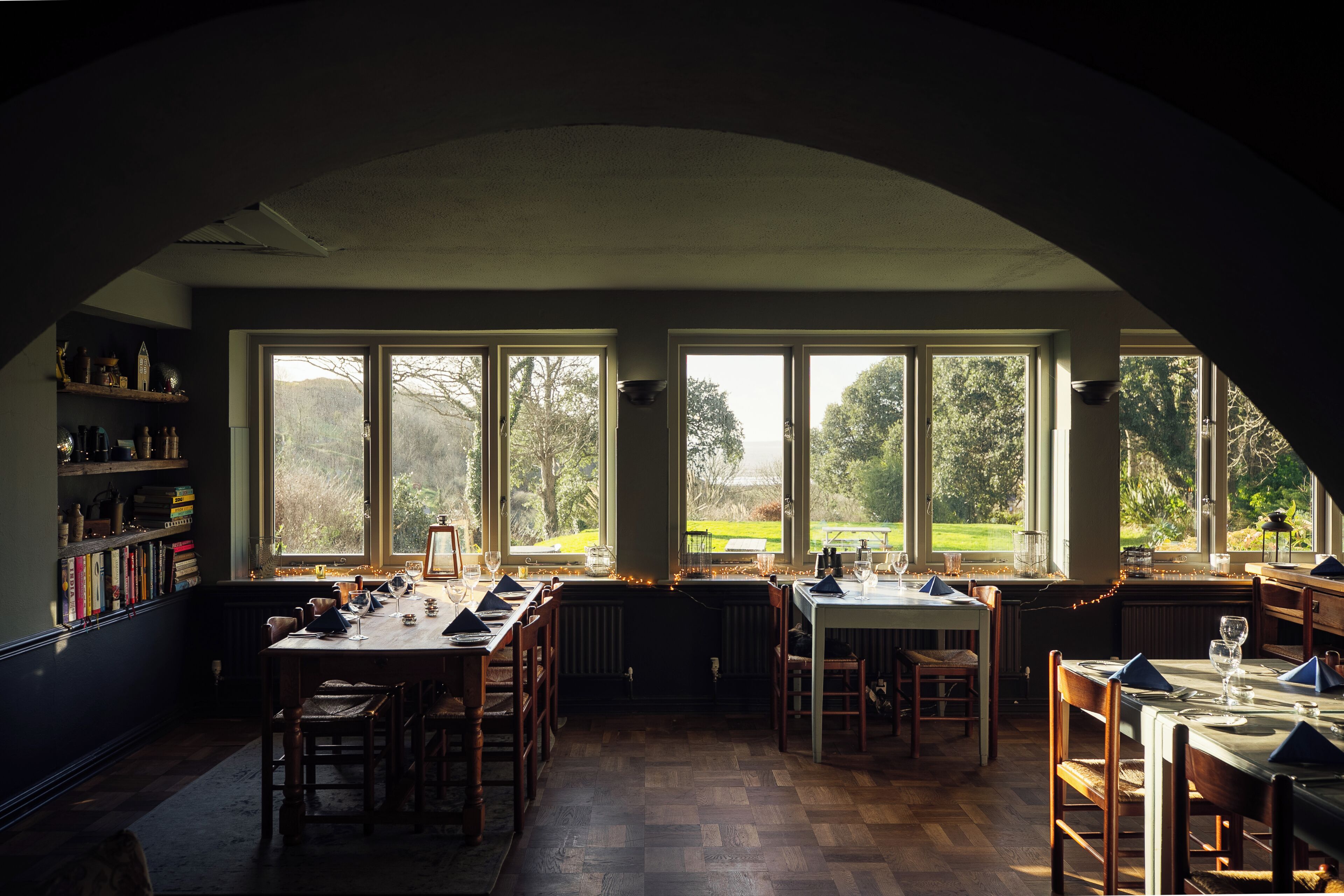 A dining area with a high ceiling, large windows, and a view of the outdoors.