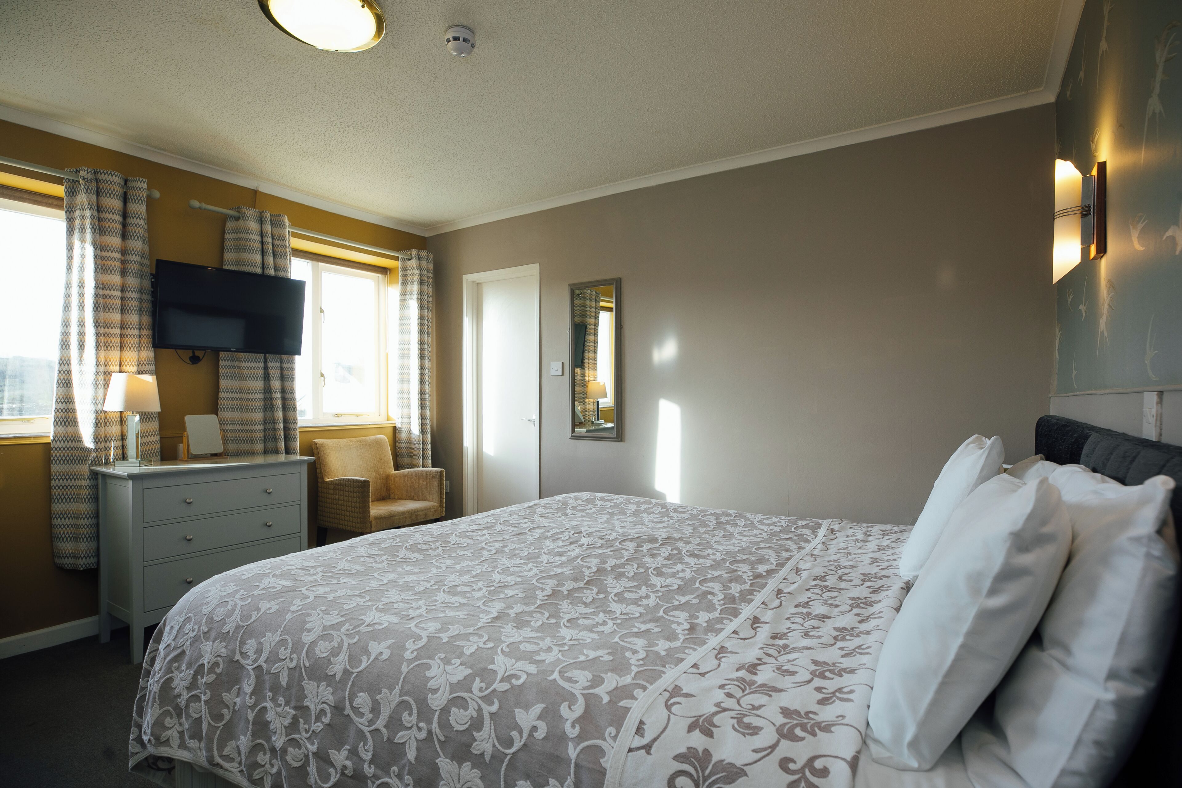 A bedroom with a bed, a dresser, a chair, a television, and a window with curtains.