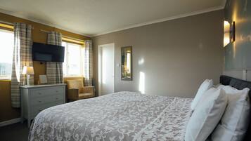 A bedroom with a bed, a dresser, a chair, a television, and a window with curtains.