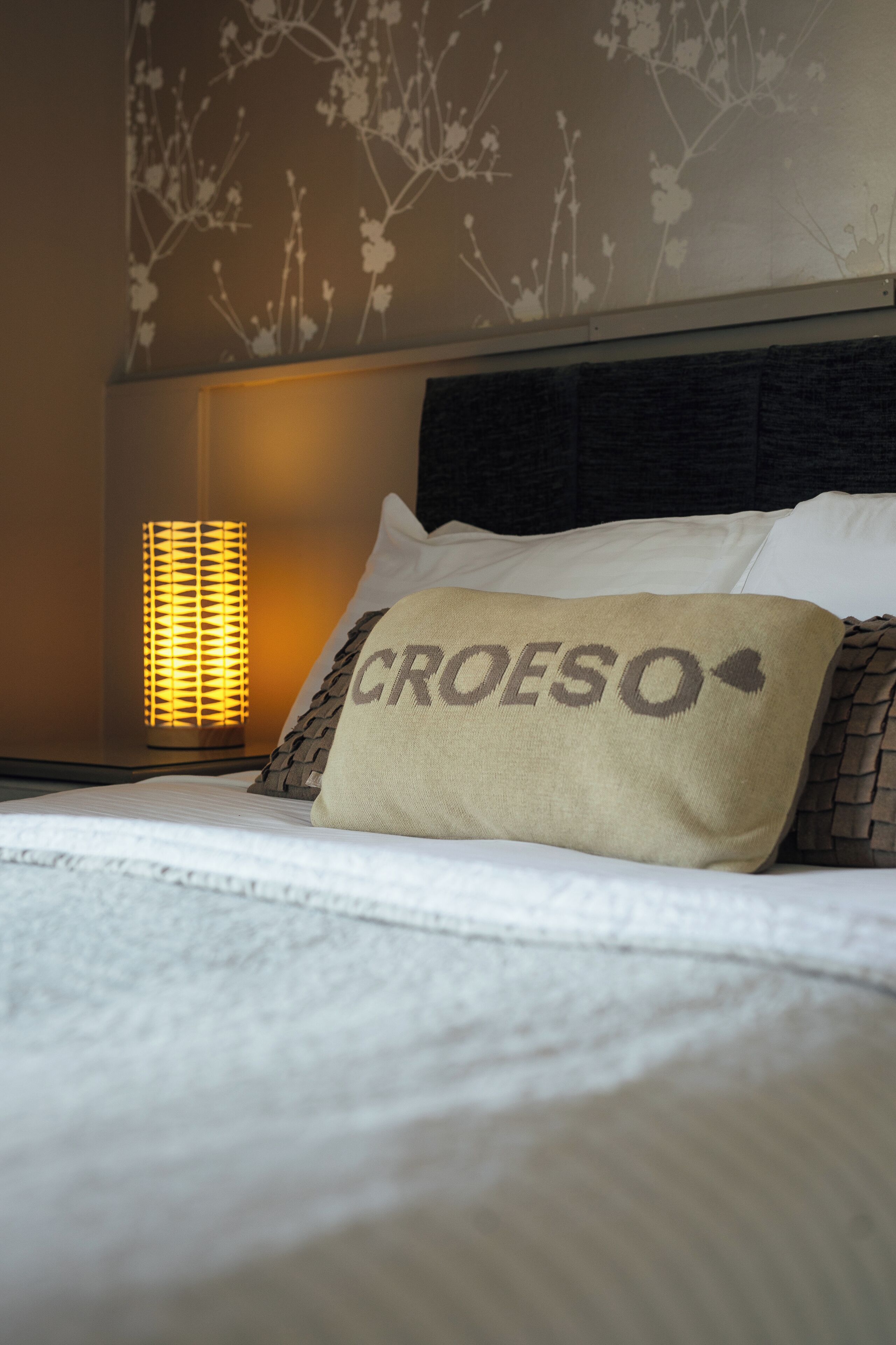 Una cama con un almohadón que dice 'CROESO' y una lámpara fijada a la pared.
