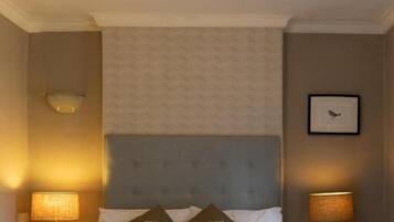 Ein ordentlich eingerichtetes Schlafzimmer mit einem Bett, zwei Nachttischen, einer Wandleuchte und einem gerahmten Bild.