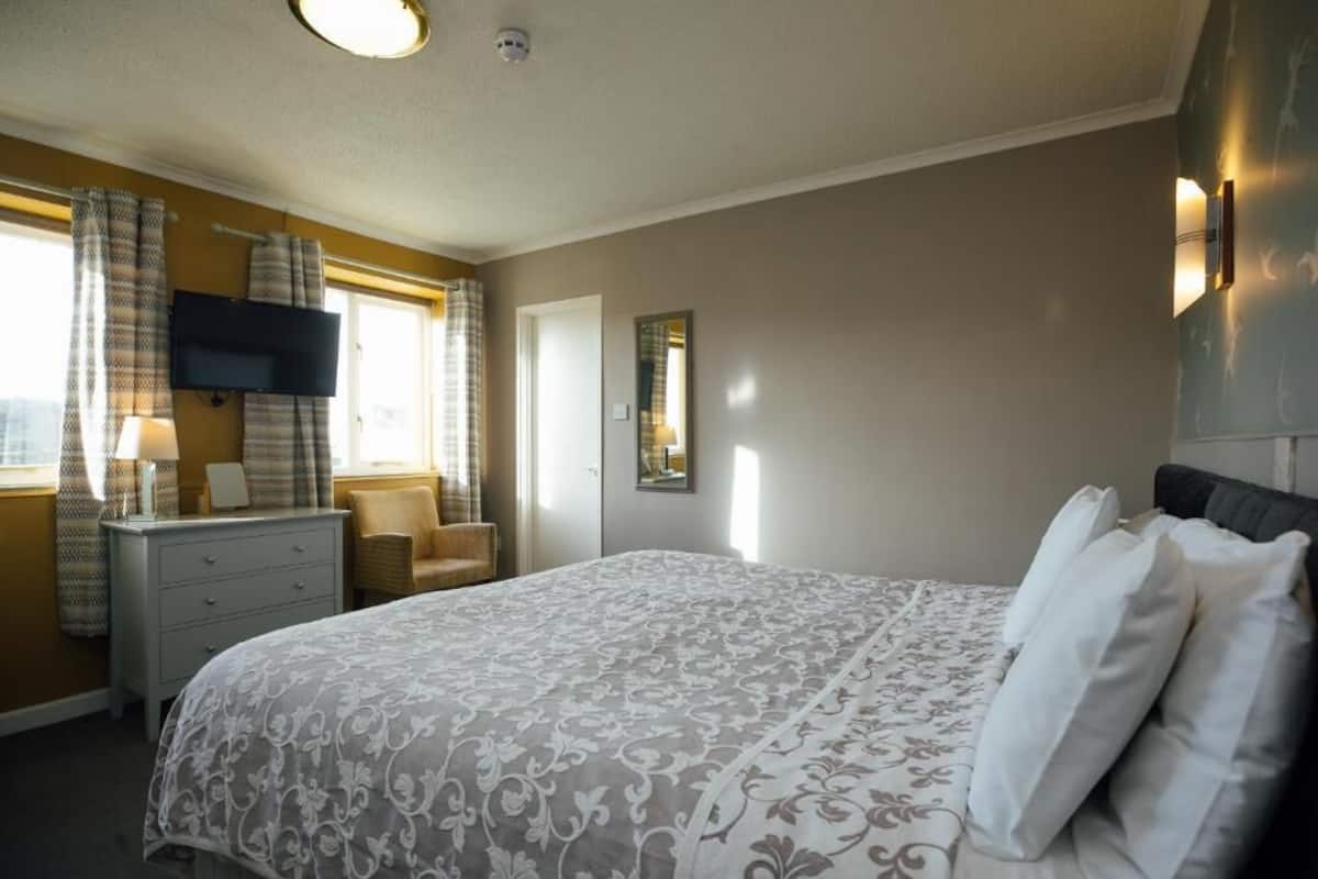 A bedroom with a bed, a dresser, a chair, a television, and a window with curtains.